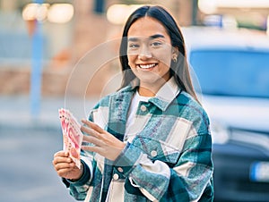 Young latin girl smiling happy counting chinese yuan banknotes at the city