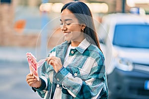 Young latin girl smiling happy counting chinese yuan banknotes at the city