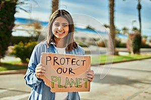 Young latin girl smiling happy holding protect our planet banner at the city