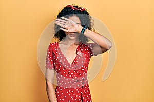 Young latin girl wearing summer dress covering eyes with arm, looking serious and sad