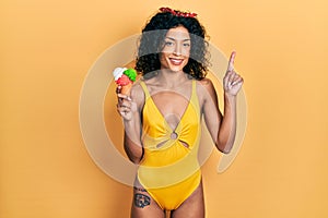 Young latin girl wearing summer style holding ice cream surprised with an idea or question pointing finger with happy face, number