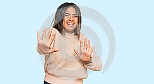 Young latin girl wearing wool winter sweater afraid and terrified with fear expression stop gesture with hands, shouting in shock