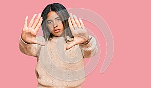 Young latin girl wearing wool winter sweater doing frame using hands palms and fingers, camera perspective