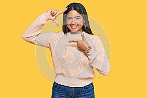 Young latin girl wearing wool winter sweater smiling making frame with hands and fingers with happy face