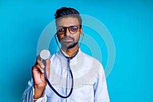 young latin hispanic medican man wear eye glasses with stethoscope in blue studio wall background