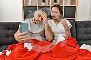 Young latin ill couple having medical teleconsultation using smartphone at home