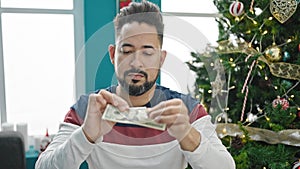 Young latin man breaking 20 dollars banknotes celebrating christmas at home