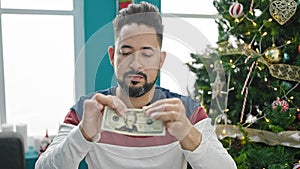 Young latin man breaking 20 dollars banknotes celebrating christmas at home