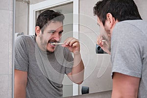 Young latin man brushing his teeth in front of the mirror in the bathroom at morning