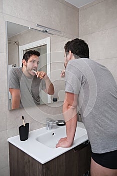 Young latin man brushing his teeth in front of the mirror in the bathroom at morning