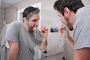 Young latin man brushing his teeth in front of the mirror in the bathroom at morning