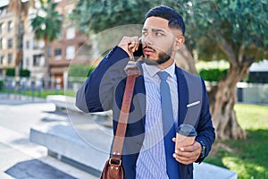Young latin man business worker talking on smartphone drinking coffee at park