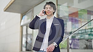 Young latin man business worker talking on smartphone looking clock at street