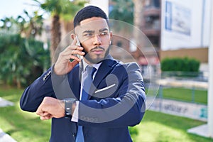 Young latin man business worker talking on smartphone looking watch at park