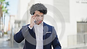 Young latin man business worker talking on smartphone looking watch at street