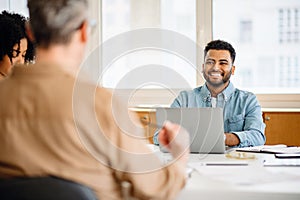 A young Latin man in casual wear, with a beaming smile participates in a meeting