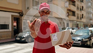 Young latin man delivery worker holding package doig coming gesture with hand at street