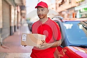 Young latin man delivery worker holding package at street