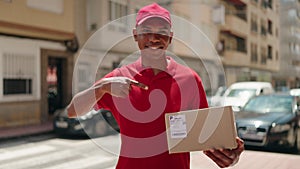 Young latin man delivery worker pointing with finger to package at street