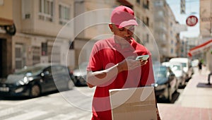 Young latin man delivery worker scanning package using smartphone at street