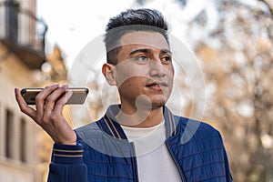 Young Latin man listening to an audio message with his smartphone