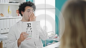 Young latin man optician examining vision with snellen test at clinic