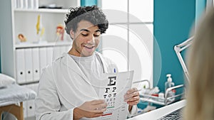 Young latin man optician examining vision with snellen test at clinic