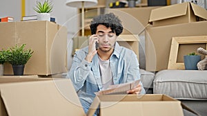 Young latin man reading document talking on smartphone looking upset at new home