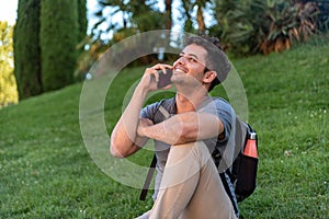 Young latin man sitting in the grass talking by mobile phone.