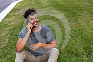 Young latin man sitting in the grass talking by mobile phone.