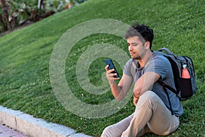 Young latin man sitting in the grass using the mobile phone.