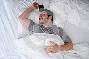 Young latin man sleeping spread out in bed with his smartphone