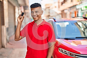 Young latin man smiling confident holding key of new car at street