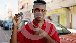 Young latin man smiling confident holding key of new car at street