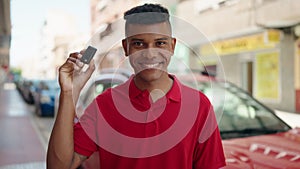 Young latin man smiling confident holding key of new car at street