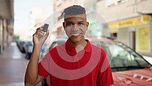 Young latin man smiling confident holding key of new car at street