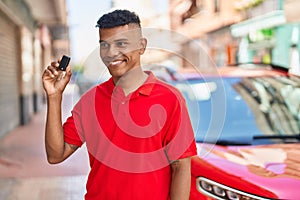 Young latin man smiling confident holding key of new car at street