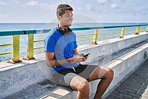Young latin man smiling happy using headphones and smartphone at the beach