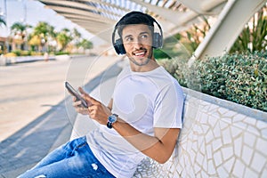 Young latin man smiling happy using smartphone and headphones sitting on the bench