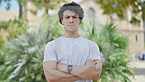 Young latin man standing with serious expression with arms crossed gesture at park