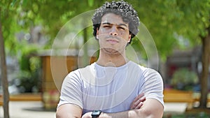 Young latin man standing with serious expression with arms crossed gesture at park