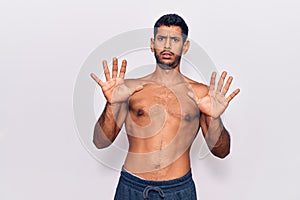 Young latin man standing shirtless afraid and terrified with fear expression stop gesture with hands, shouting in shock