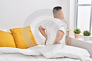 Young latin man suffering for back injury sitting on bed at bedroom