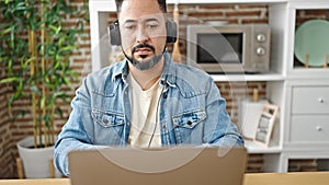 Young latin man using laptop and headphones sitting on table at dinning room