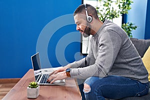 Young latin man using laptop and headphones sitting on table at home