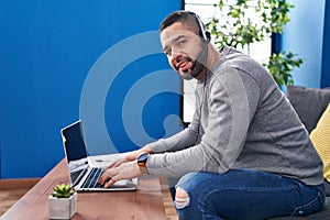 Young latin man using laptop and headphones sitting on table at home