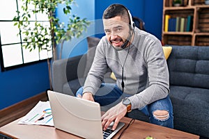 Young latin man using laptop and headphones sitting on table at home