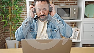 Young latin man using laptop wearing headphones sitting on table at dinning room