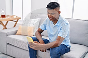 Young latin man using smartphone sitting on sofa at home