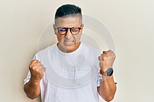 Young latin man wearing casual clothes and glasses celebrating surprised and amazed for success with arms raised and eyes closed